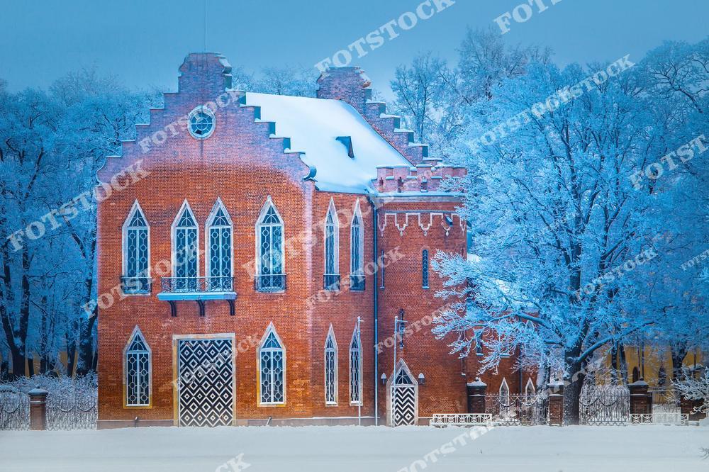 На фотографии изображено Адмиралтейство в Екатерининском парке города Пушкин (Царское Село), выполненное в стиле неоготики. Красный кирпичный фасад здания ярко выделяется на фоне покрытых инеем деревьев. Это архитектурное сооружение напоминает небольшой замок и является одной из самых атмосферных достопримечательностей парка. Зимнее убранство добавляет сказочности, делая это место особенно живописным и привлекательным для туристов.